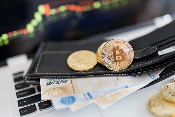 Eine Laptop-Tastatur, auf der eine Brieftasche mit Bitcoin-Münzen und Bitcoin-Papierwallets liegen.